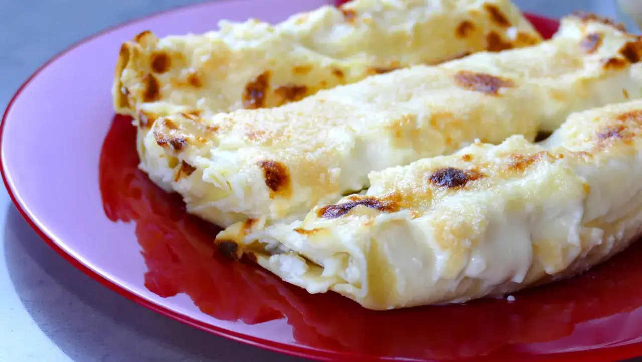 Cannelloni di carne ricetta della nonna, dorati e filanti, serviti su un piatto rosso.