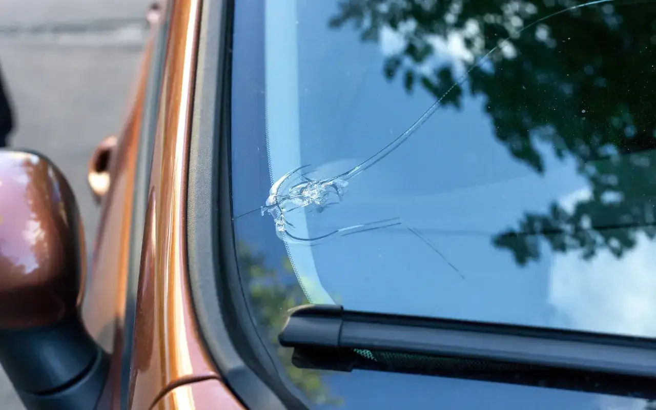 Un impact de gravillon a laiss&eacute; une &eacute;toile sur le pare brise fissur&eacute; d'une voiture couleur cuivre.