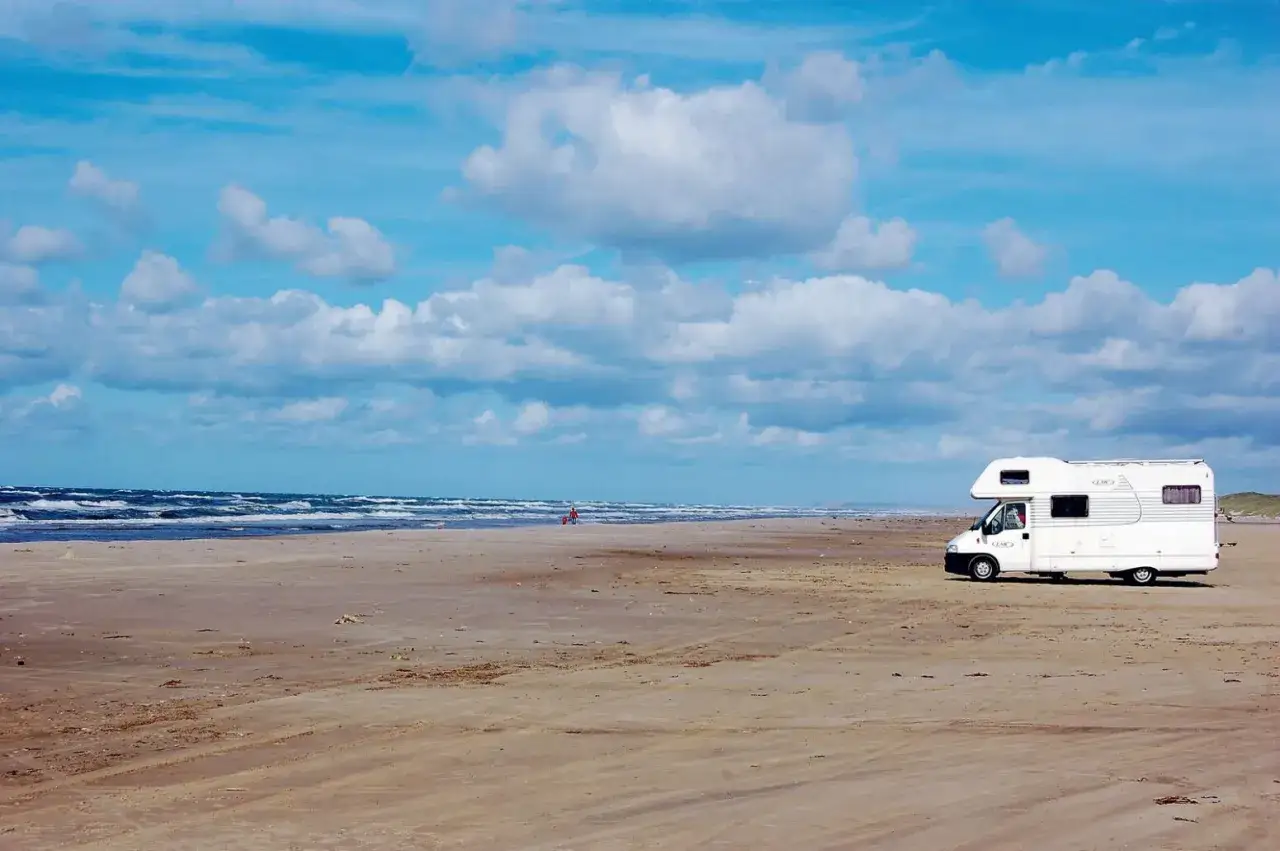 Husbil p&aring; en sandstrand vid havet. En person syns i fj&auml;rran. En perfekt plats att bes&ouml;ka Jylland p&aring;.