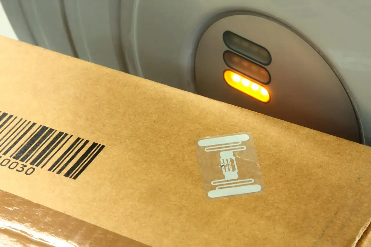 Pudełko z kodem kreskowym i naklejką kod rfid zbliża się do czytnika z zapalonymi diodami.
