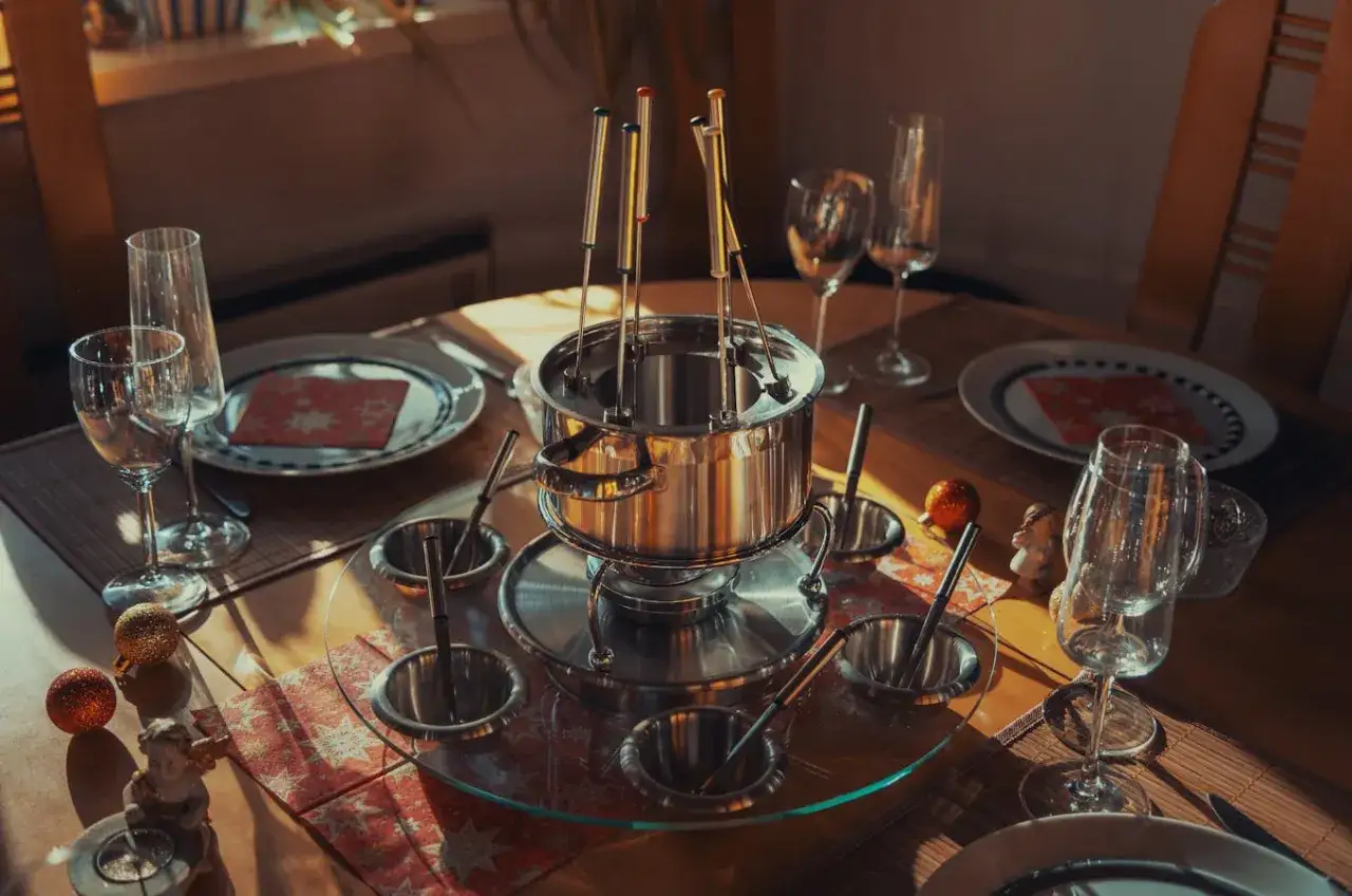 Table dress&eacute;e pour une fondue chinoise, avec un appareil &agrave; fondue, des bols, des assiettes et des verres. Le vin attend patiemment.