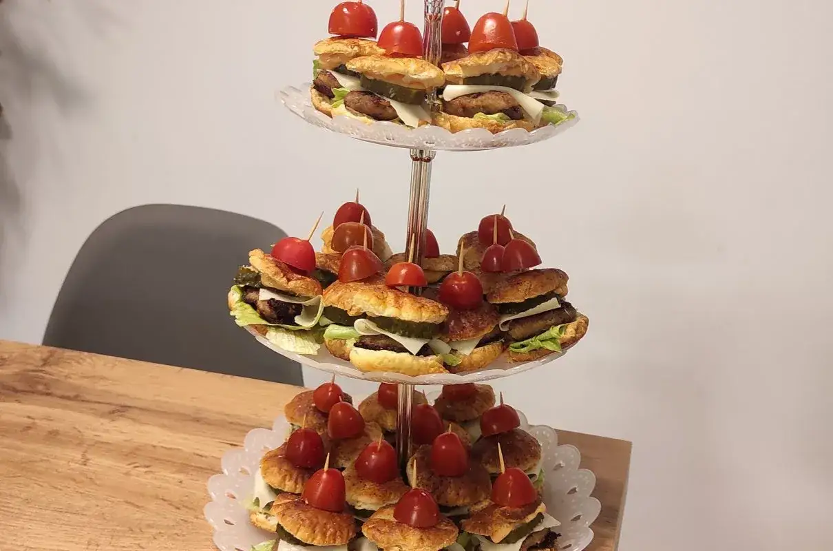 Mini burgery z ciasta francuskiego, ułożone na paterze, z pomidorkami koktajlowymi na wierzchu.