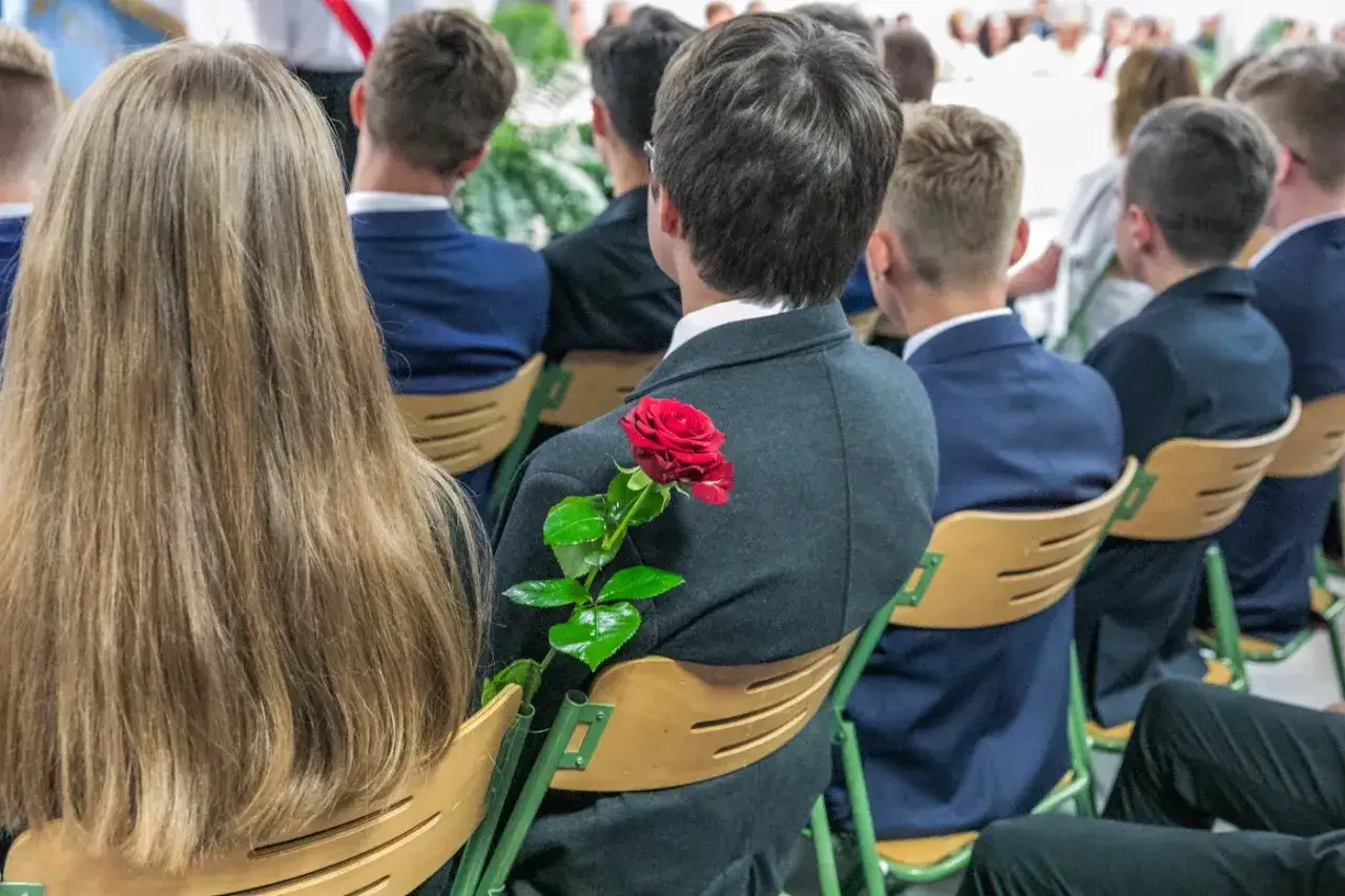 Uczniowie w garniturach, jeden z nich z czerwoną różą. Czy w technikum jest matura? To pytanie zadają sobie młodzi ludzie przed ważnym egzaminem.