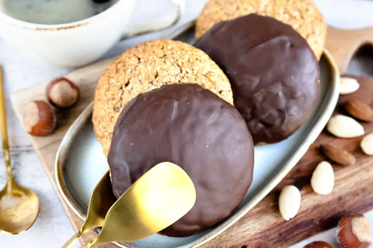 Schokoladen-Elisenlebkuchen auf einem Teller, daneben Nüsse und eine Kaffeetasse. Ein köstliches Rezept für Elisenlebkuchen.