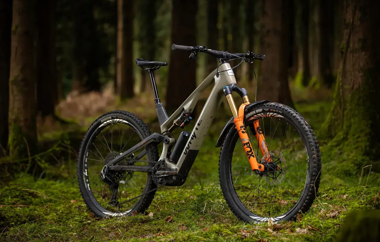 A Yeti MTE e-bike rests on mossy ground in a forest, its olive green frame and bright orange Fox suspension ready for adventure.
