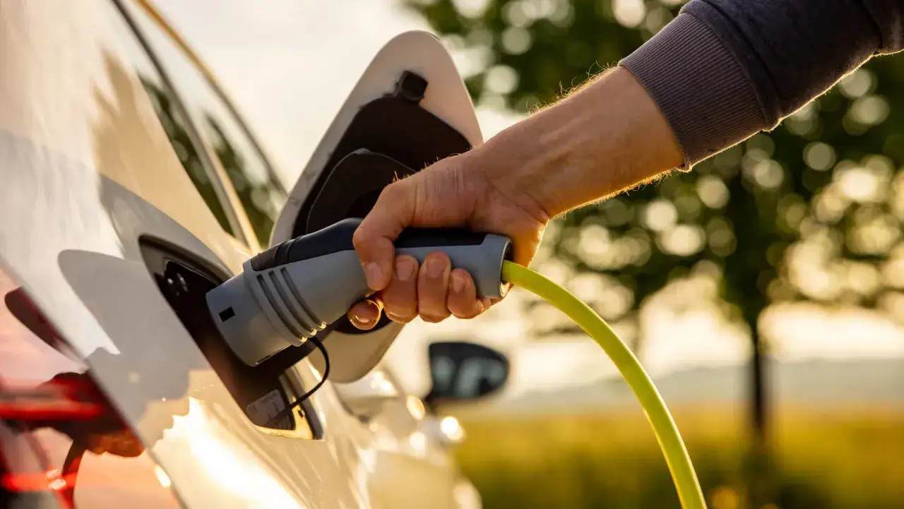 Dłoń podłącza ładowarkę do białego samochodu elektrycznego Fisker.
