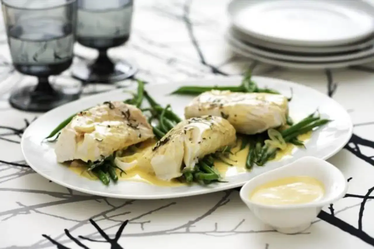Tre bitar vit fisk med gr&ouml;na b&ouml;nor och en kr&auml;mig beurre blanc-s&aring;s.