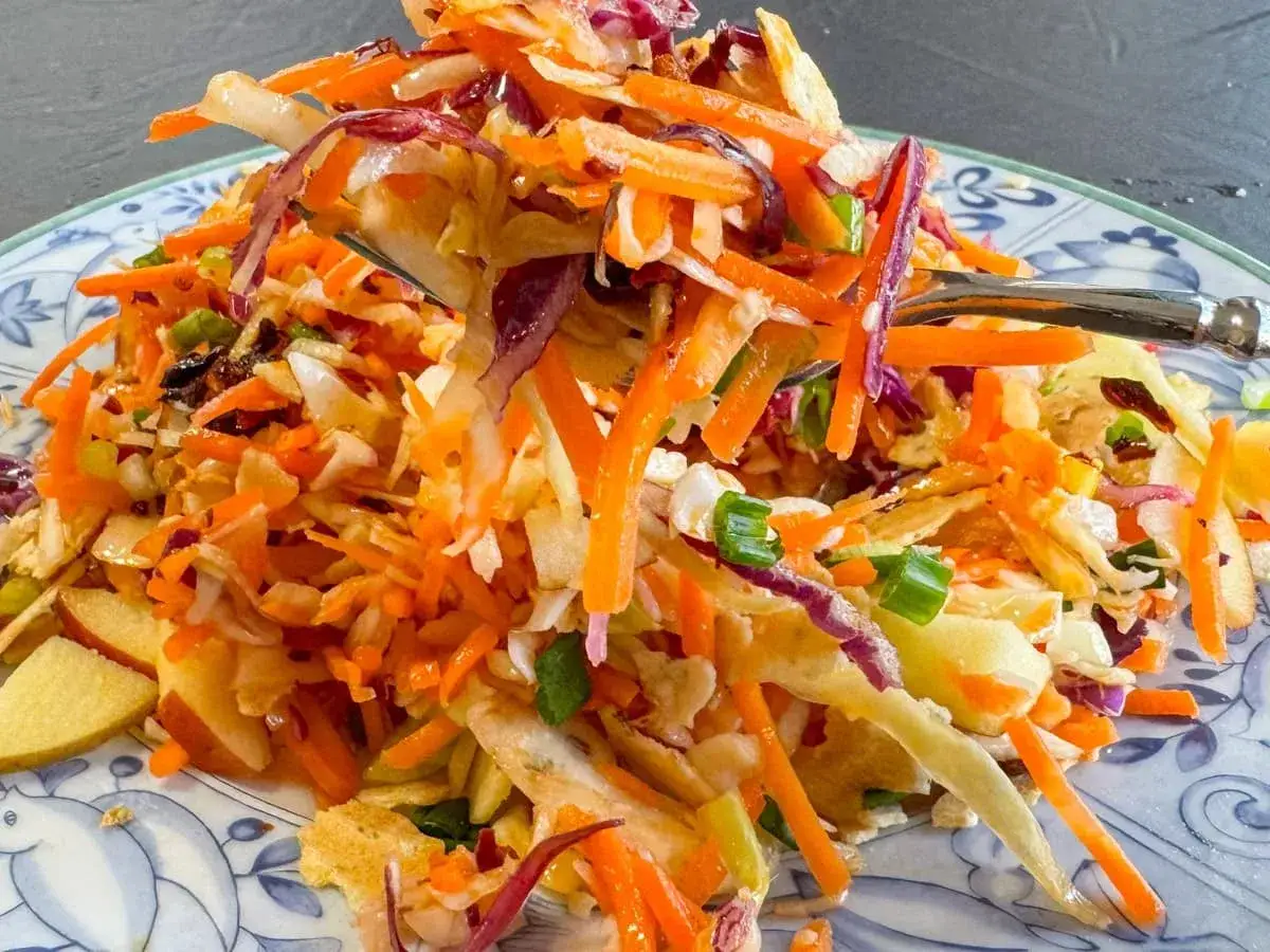 En h&auml;rlig asiatisk k&aring;lsallad med strimlad vitk&aring;l, mor&ouml;tter, r&ouml;dl&ouml;k och salladsl&ouml;k, serverad p&aring; en bl&aring;vit tallrik.
