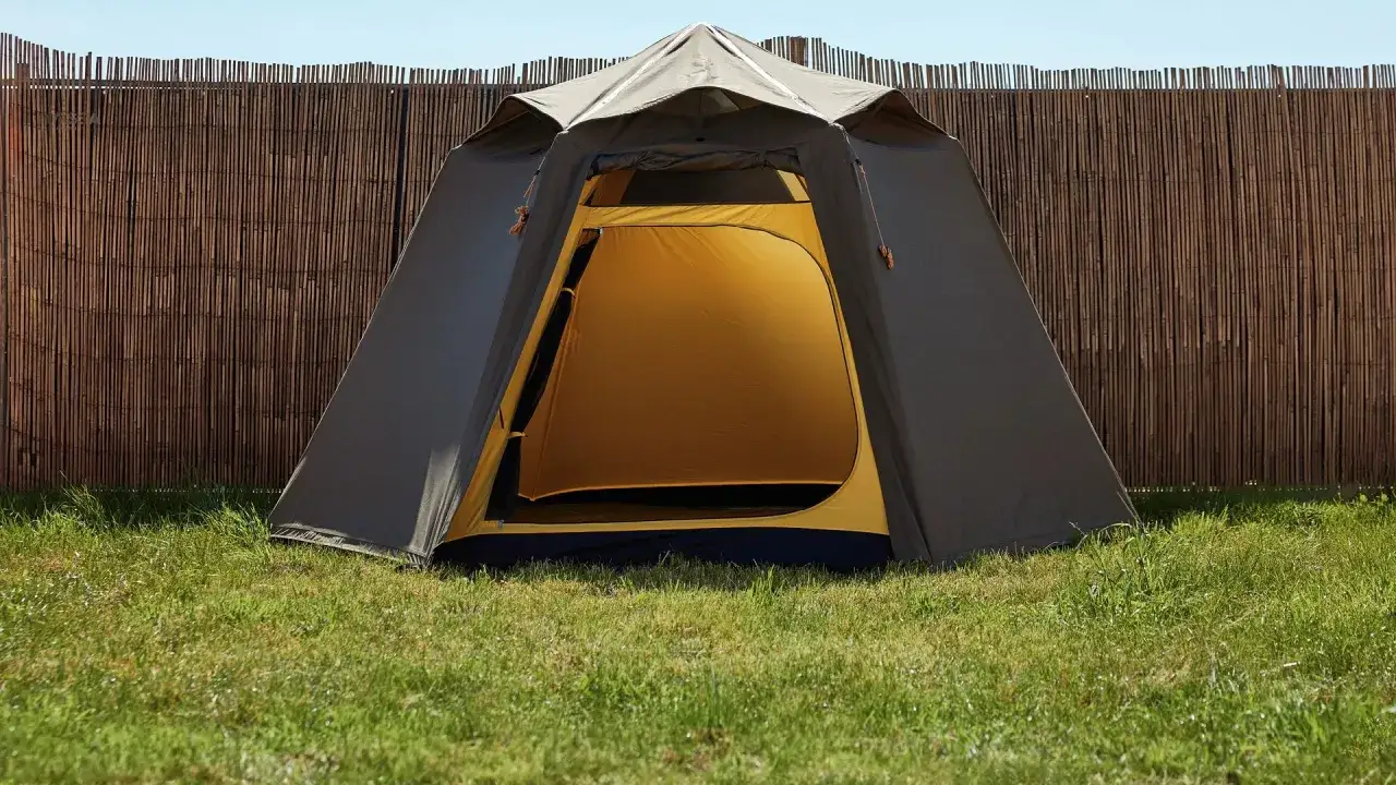 Ein Zelt steht auf einer gr&uuml;nen Wiese vor einem Bambuszaun. Perfekt f&uuml;r die Parookaville Packliste!