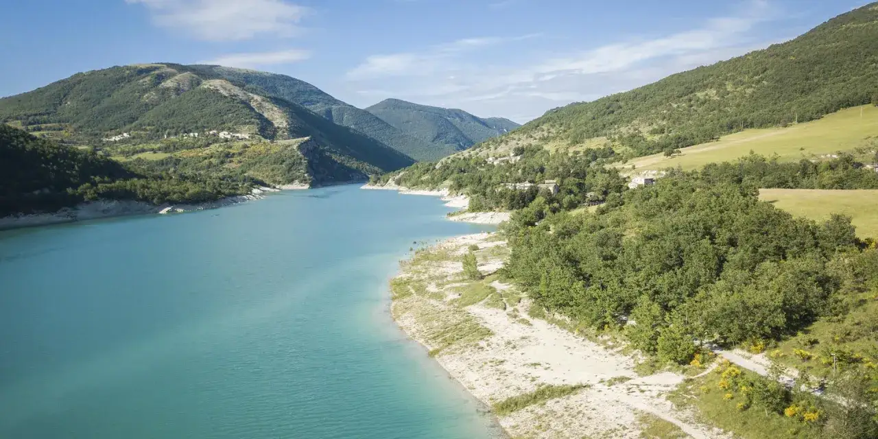 Il **lago di Fiastra** incanta con le sue acque turchesi, circondato da colline verdi e piccoli borghi.