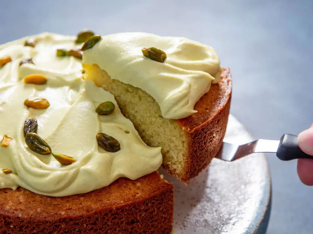 Un trozo de pastel esponjoso cubierto con una generosa capa de crema pistacho y decorado con pistachos enteros.