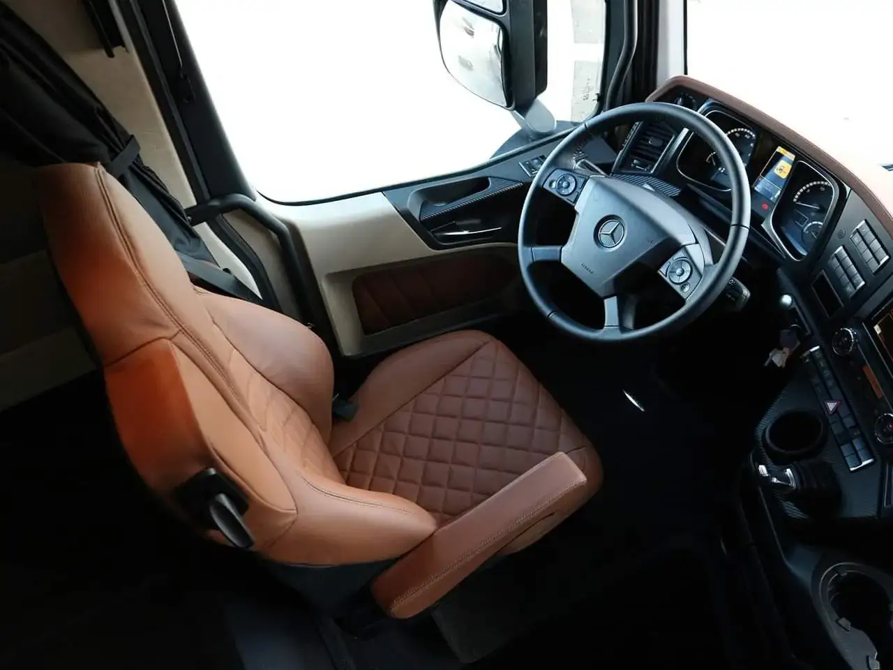 Wnętrze luksusowego Mercedesa Actros MP4 z brązową, pikowaną tapicerką siedzenia i kierownicą.