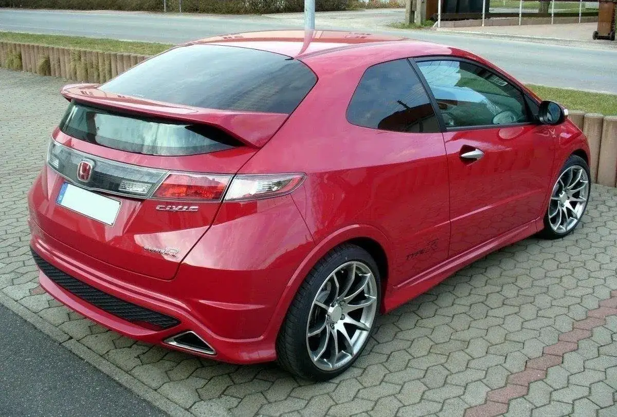 Czerwony Honda Civic VIII Type R z charakterystycznym spoilerem na klapie bagażnika, zaparkowany na kostce brukowej.