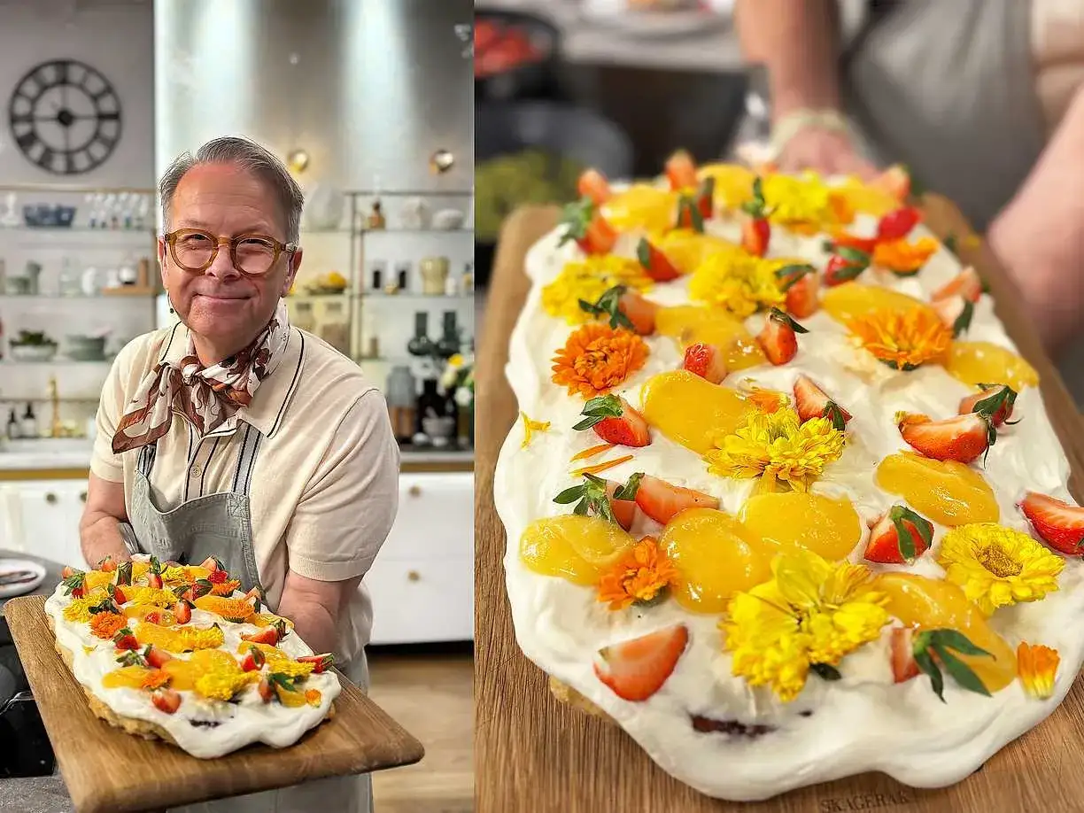 Glad kock visar upp en vacker p&aring;skt&aring;rta i l&aring;ngpanna, dekorerad med jordgubbar, aprikoser och gula blommor.