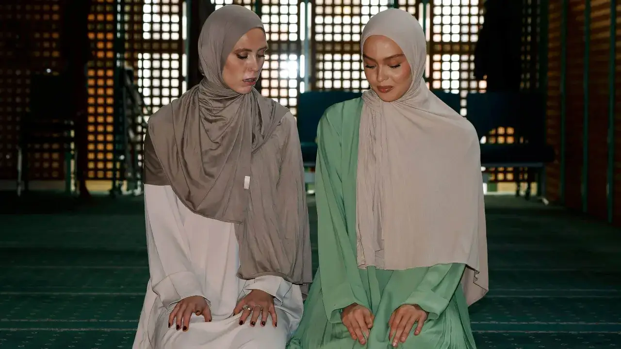 Tv&aring; kvinnor i hijab kn&auml;b&ouml;jer p&aring; en gr&ouml;n matta i en mosk&eacute;, f&ouml;rberedda f&ouml;r qiyam al layl.