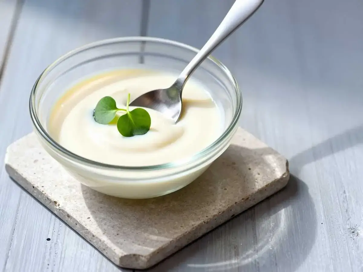 Cremiges Joghurt Dressing in einer Glasschale, garniert mit einem grünen Blatt. Ein Löffel ruht darin.