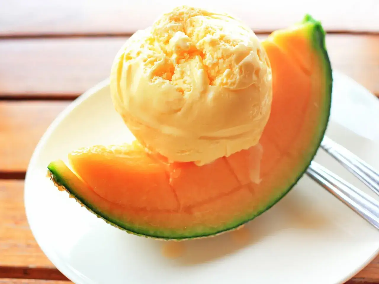 Ein Löffel cremiges Meloneneis auf einem saftigen Cantaloupe-Melonenstück. Perfekt, um Meloneneis selber machen zu lernen und den Sommer zu genießen.