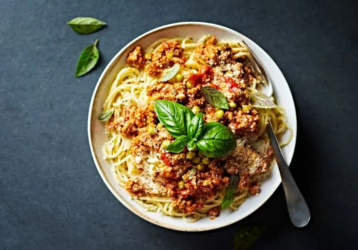 Spaghetti con piselli z bogatym sosem mięsnym, groszkiem i świeżą bazylią, posypane parmezanem.