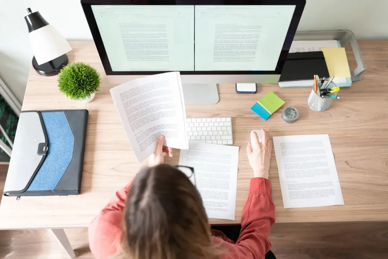 Kobieta pracuje przy biurku, analizując dokumenty. To praca copywritera, który tworzy teksty.