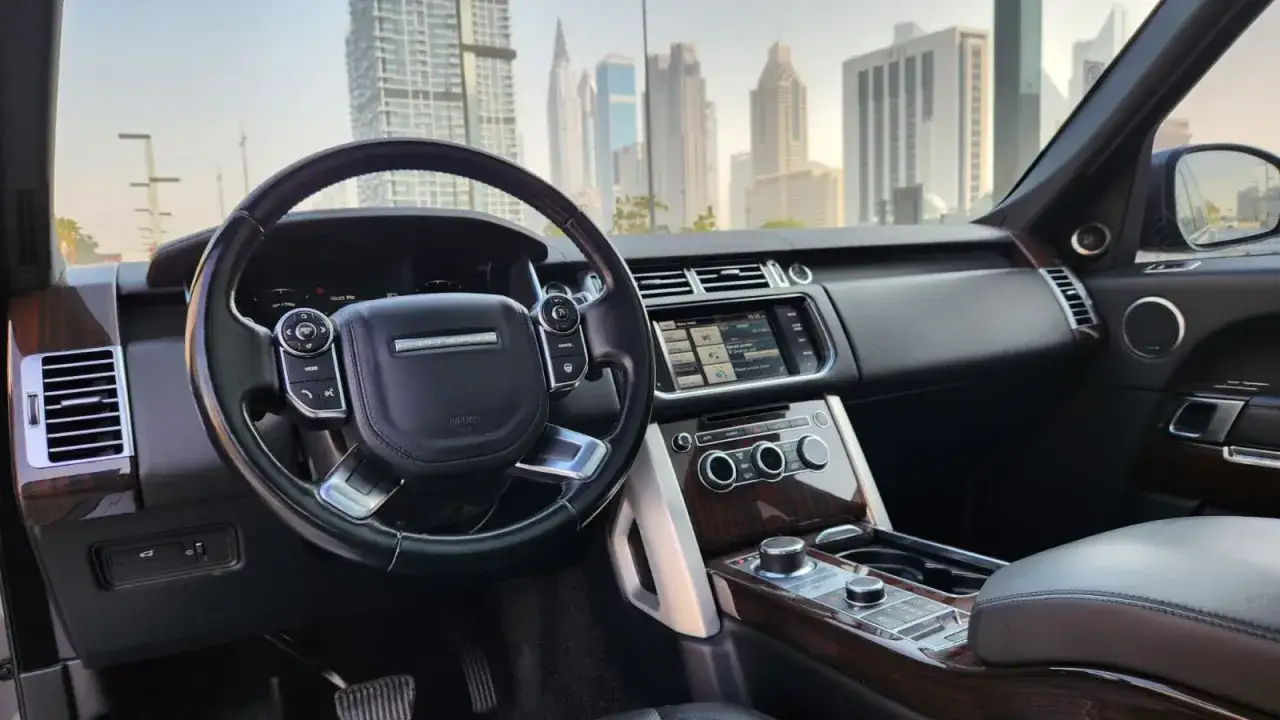 Wnętrze Range Rover Vogue z widokiem na drapacze chmur. Luksusowe detale, skóra i drewno.