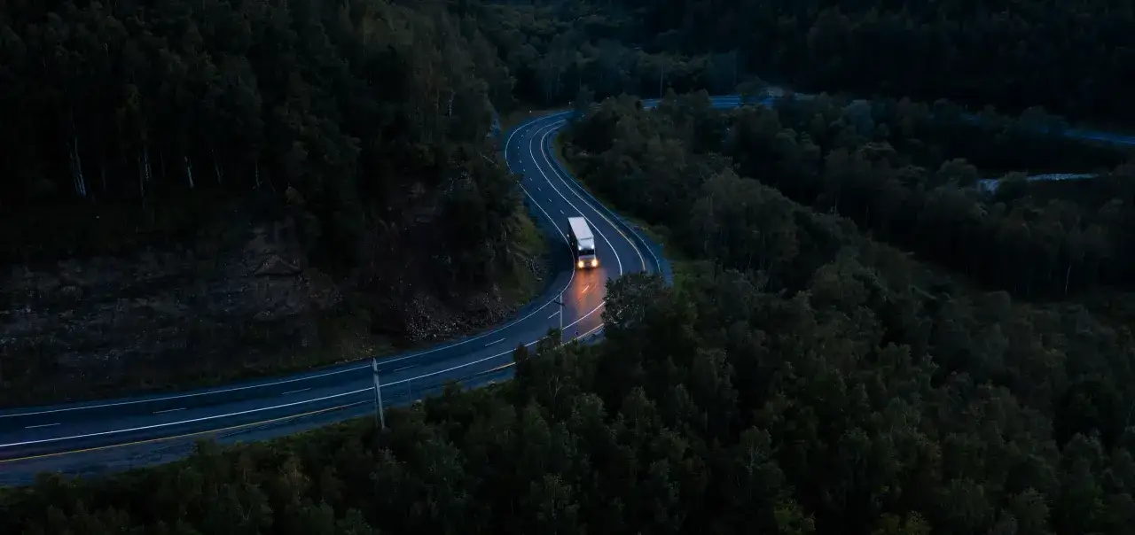 Ein einsamer LKW f&auml;hrt auf einer kurvigen Autobahn nachts durch einen dunklen Wald.