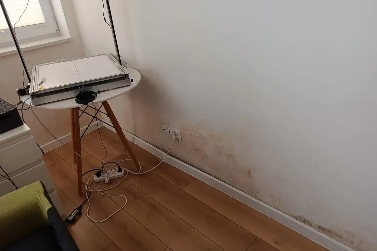 Ślady wilgoci na ścianie, typowe dla patodeweloperki, obok stołu z elektroniką.