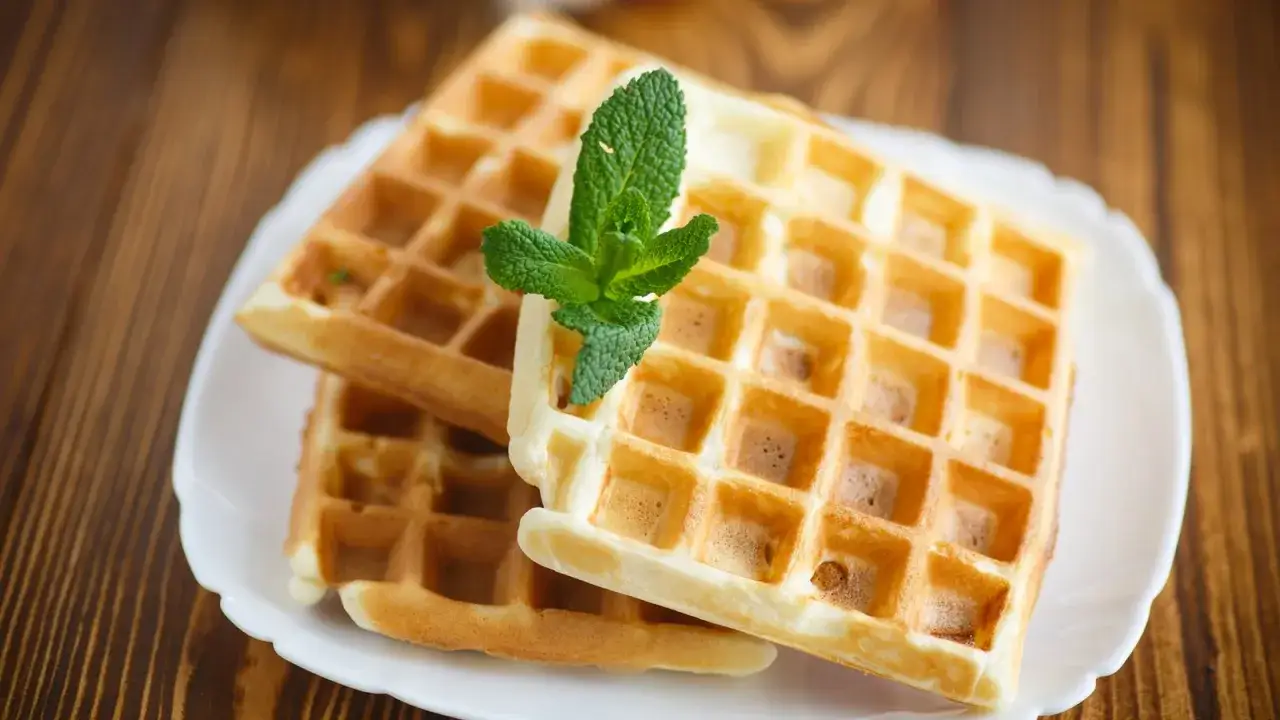 Zwei goldbraune Waffeln ohne Backpulver, garniert mit frischer Minze, auf einem wei&szlig;en Teller.
