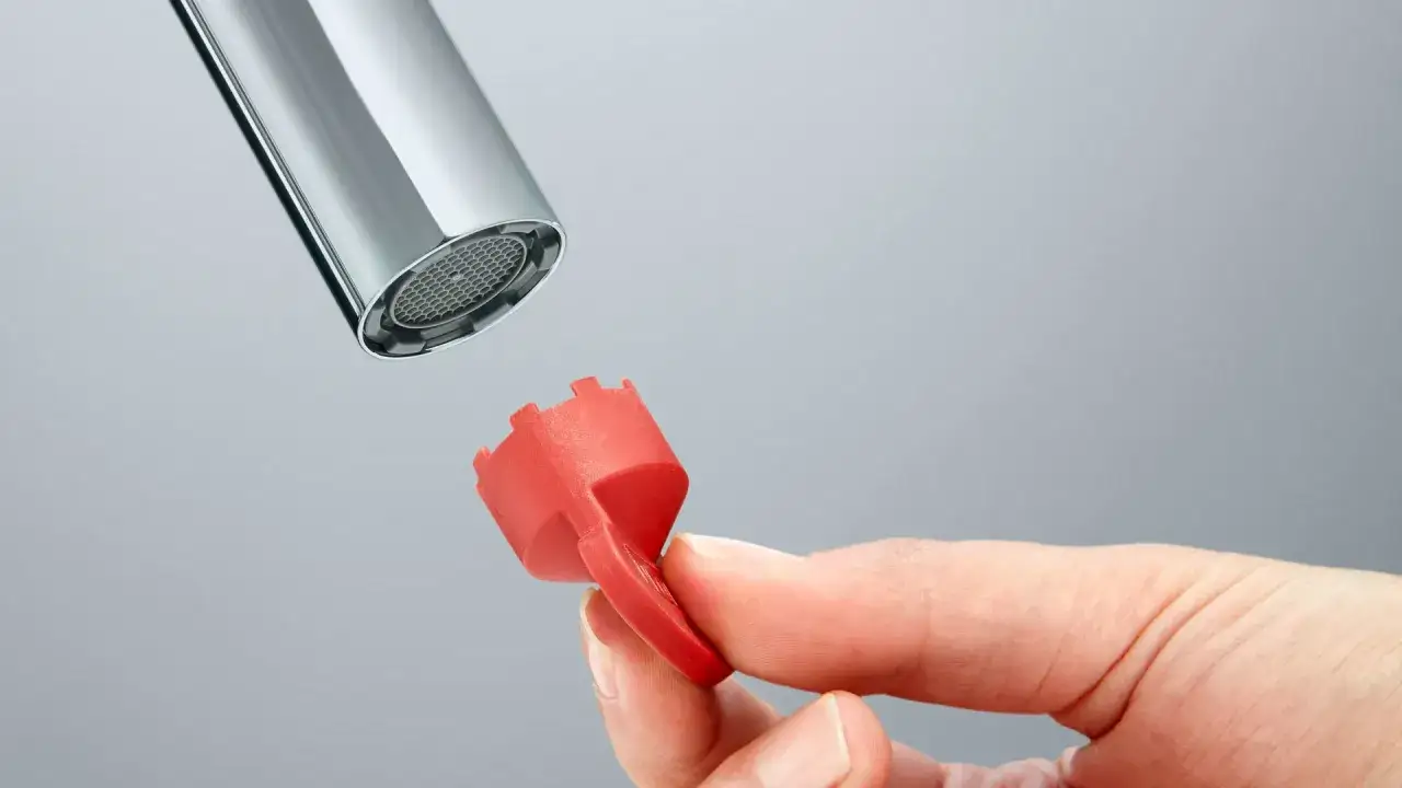 Roter Schlüssel zum Wasserhahn Sieb reinigen wird gehalten.