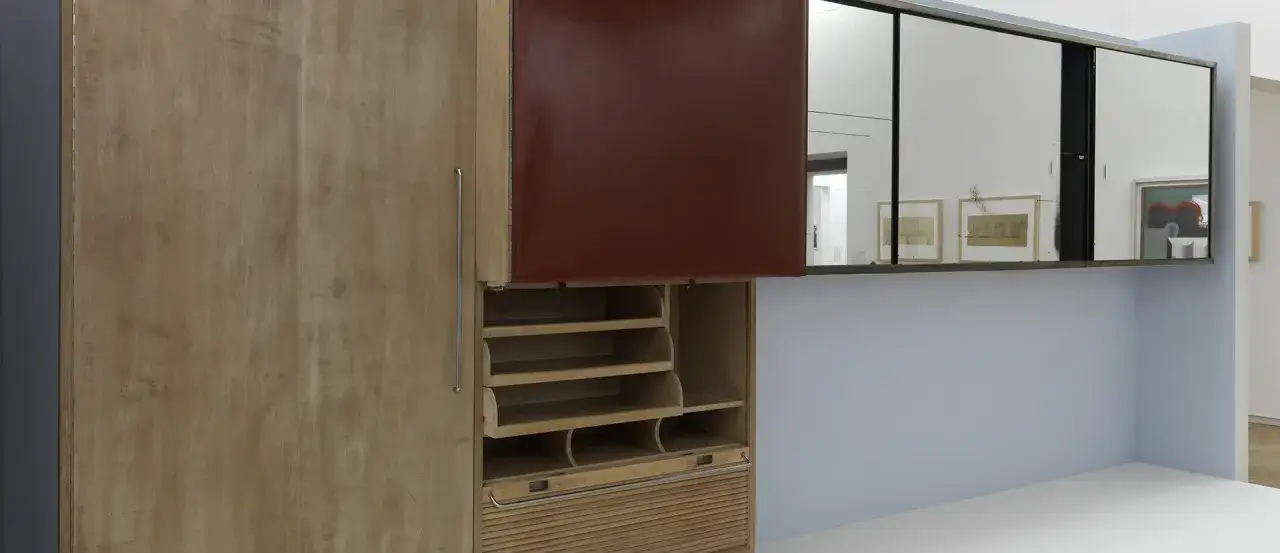 Meuble de rangement en bois clair avec porte bordeaux, étagères et volet roulant, une création de Louis Sognot.