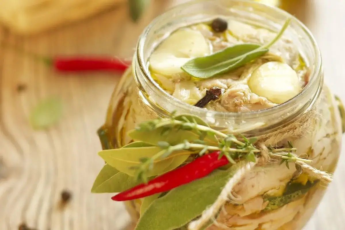 Tonno di coniglio in olio, con erbe aromatiche, peperoncino e spezie, in un barattolo di vetro decorato.