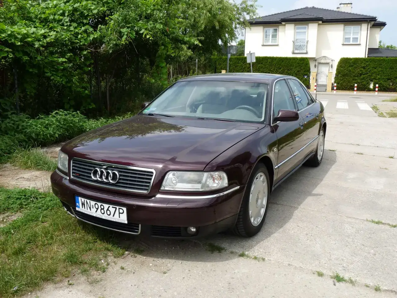 Elegancki, bordowy Audi A8 D2 4.2 z lat 90. stoi przed nowoczesnym domem.