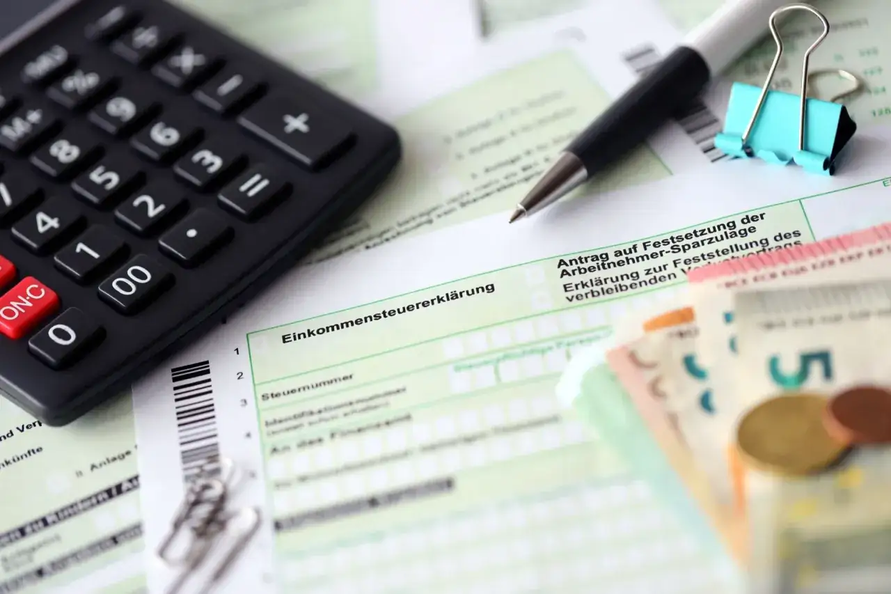 Steuererklärung mit Rechner, Stift und Geld. So lassen sich Umzugskosten steuerlich geltend machen.