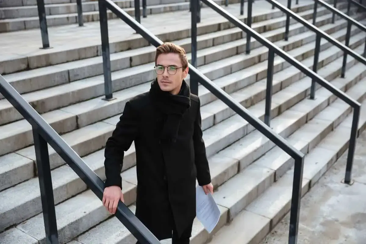 Hombre con gafas y abrigo negro sube escaleras de piedra, un ejemplo de dise&ntilde;o de escalera moderno.