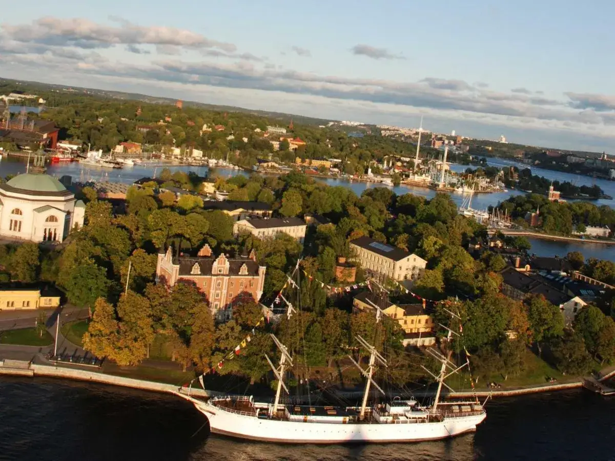 Vacker vy &ouml;ver Djurg&aring;rden med skeppet af Chapman i f&ouml;rgrunden, omgivet av gr&ouml;nska och historiska byggnader.