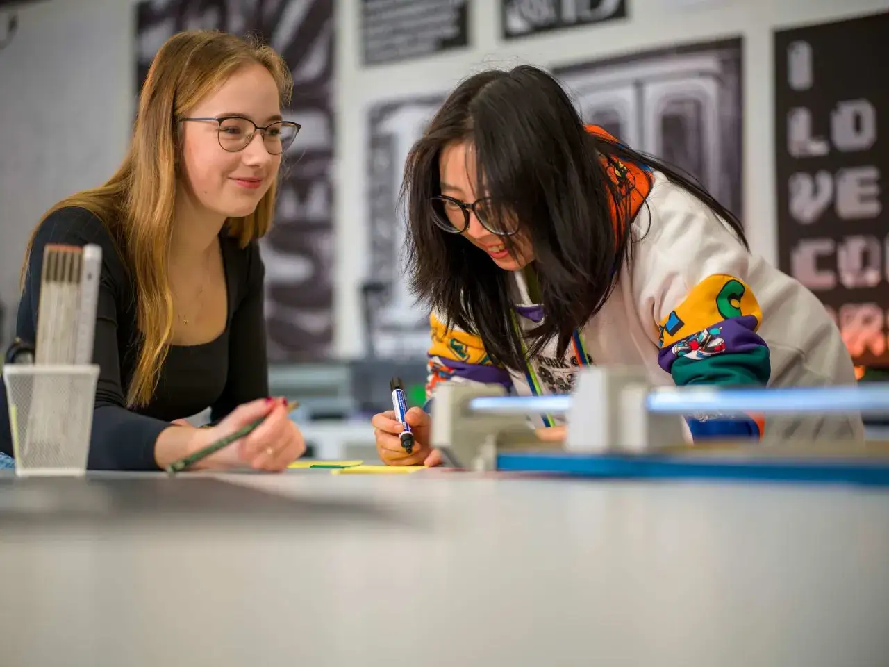 Zwei Studentinnen im Publizistik Studium arbeiten konzentriert an einem Projekt. Eine h&auml;lt einen Stift, die andere einen Marker.