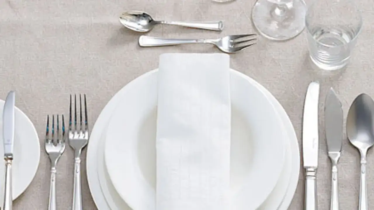 Festlich gedeckter Tisch: besteck auflegen nur messer und gabel, weiße Teller, Stoffserviette, Glas und Wasser.