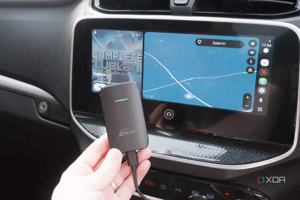 Adattatore per android auto wireless in mano, con schermo auto che mostra navigazione e musica.