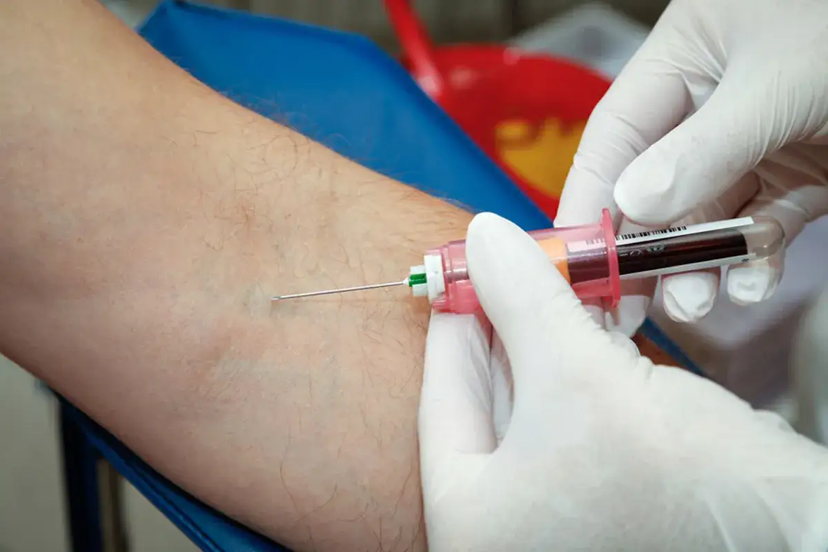 Une infirmi&egrave;re effectue une piqure pour une prise de sang sur le bras d'un patient. Le sang remplit le tube.