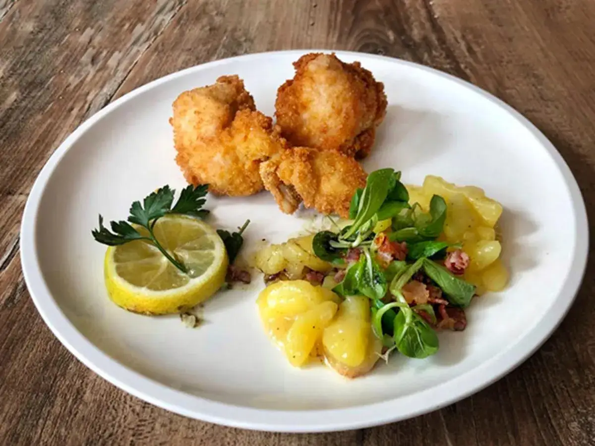 Knuspriges Wiener Backhendl Original Rezept mit Kartoffelsalat und Zitrone auf weißem Teller.