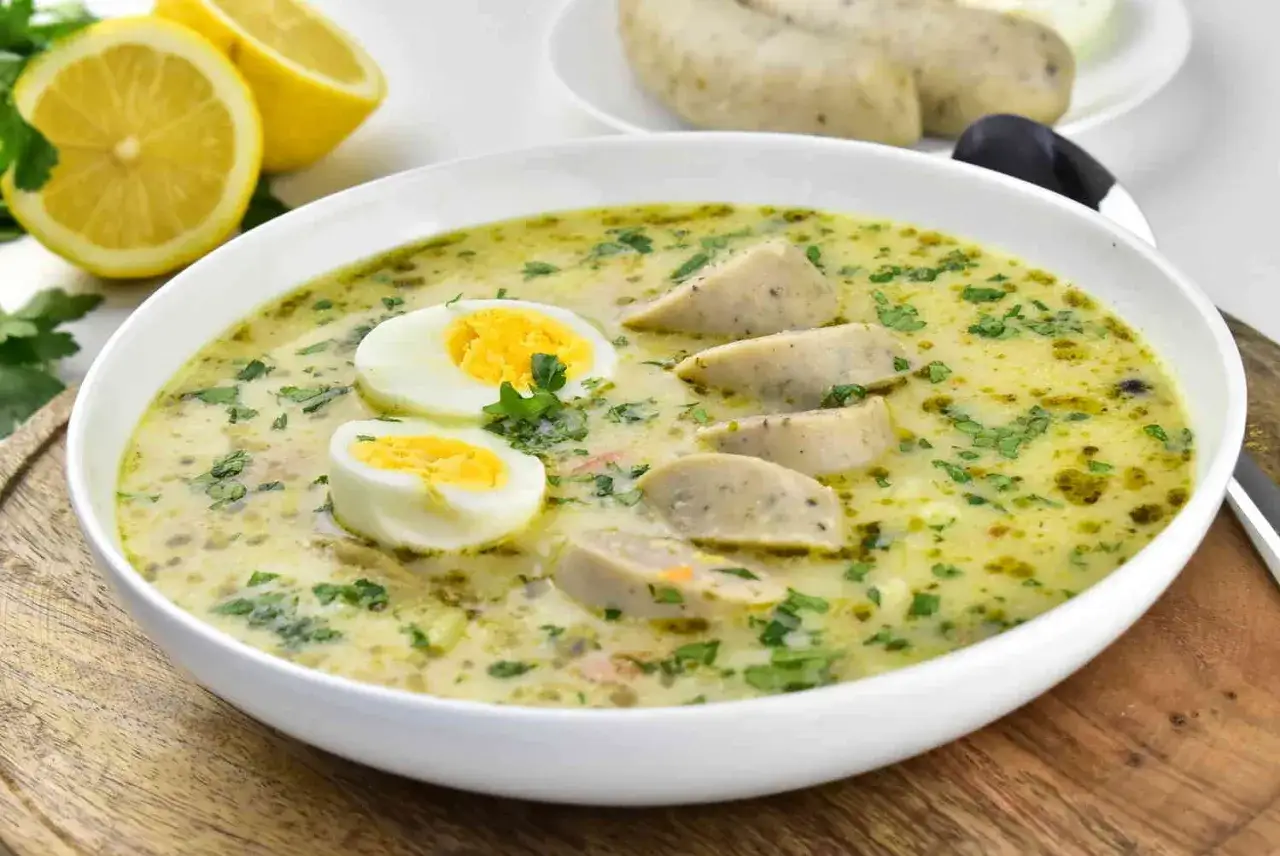 Aromaticzny barszcz chrzanowy z jajkiem i kiełbasą, ozdobiony natką pietruszki. Obok cytryny i białe kiełbaski.