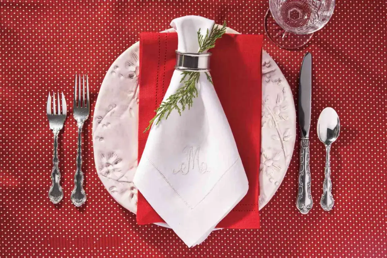 Une table dressée pour Noël avec un pliage de serviette élégant orné d'une branche de sapin.