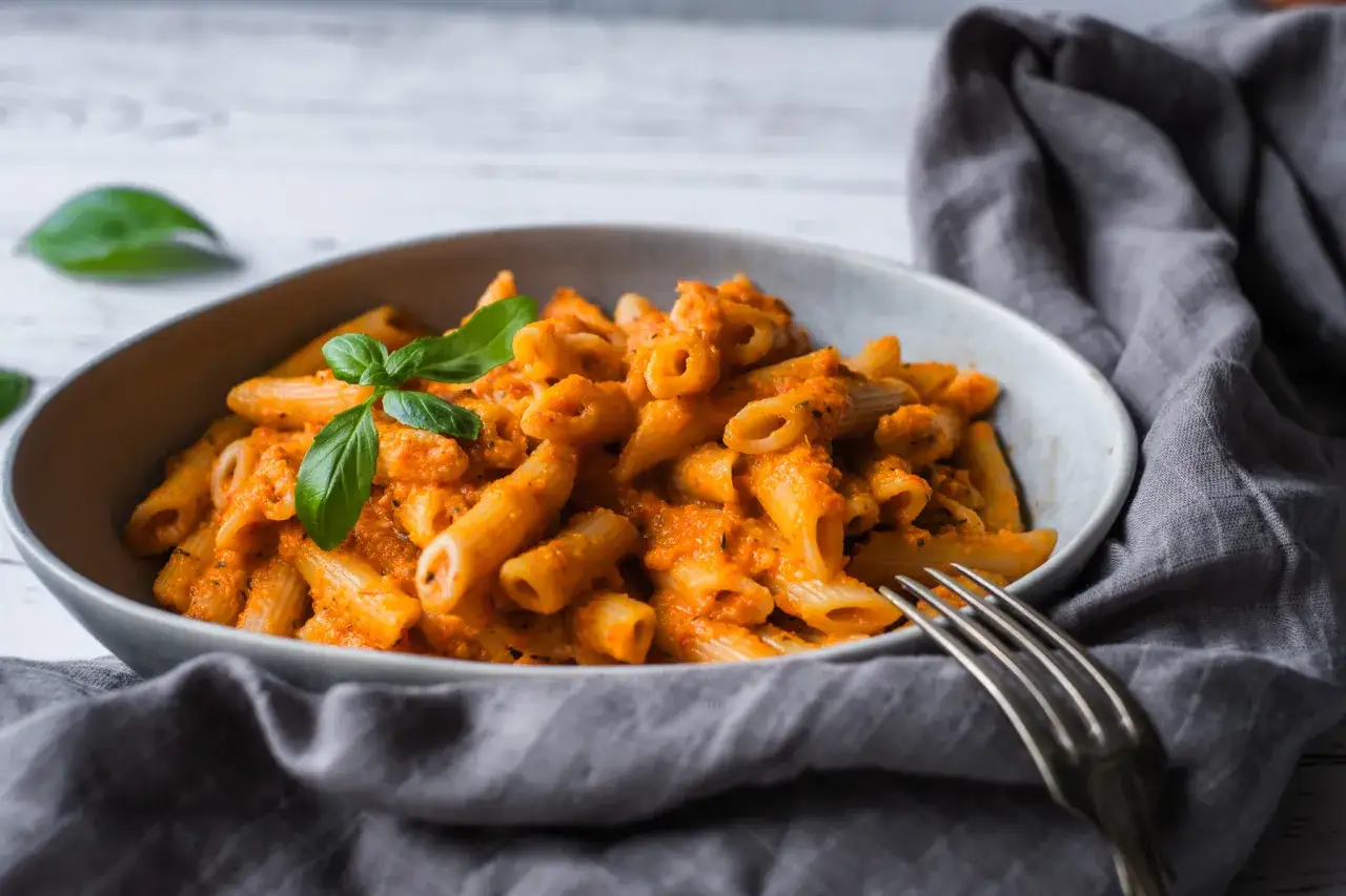 En skål med krämig vegetarisk pasta med en krallig tomatsås och färsk basilika. En gaffel ligger bredvid.