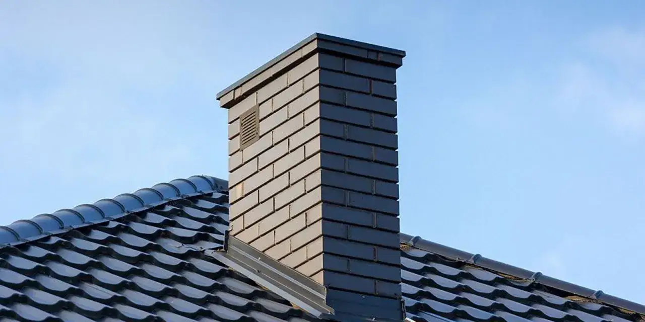 Nowoczesny, ceglany komin do kominka na tle błękitnego nieba. Elegancki element dachu.
