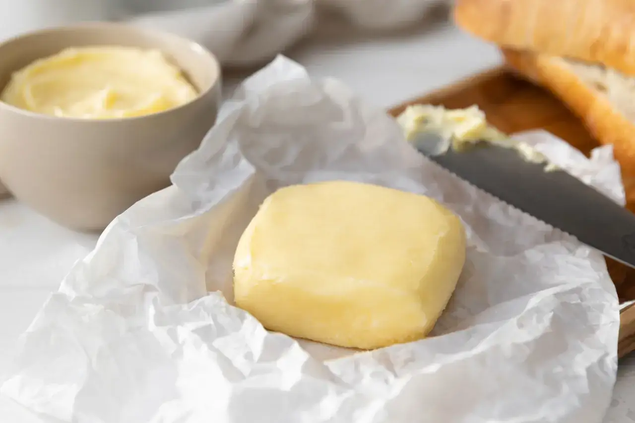 Frisch gemachte Butter auf Backpapier, daneben eine Sch&uuml;ssel mit Butter und ein Messer mit Brot. So einfach kann butter selber machen sein!