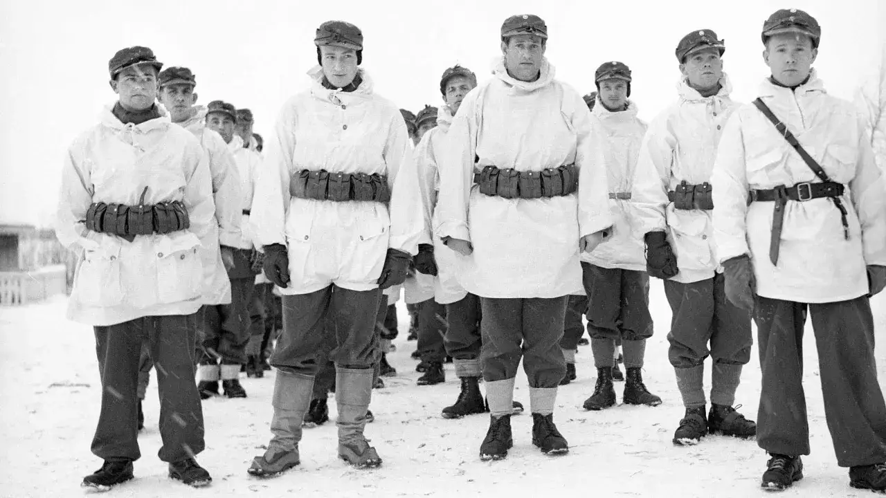 Soldater i vita vinteruniformer, med Allan Mann i t&auml;ten, st&aring;r uppradade i sn&ouml;n.