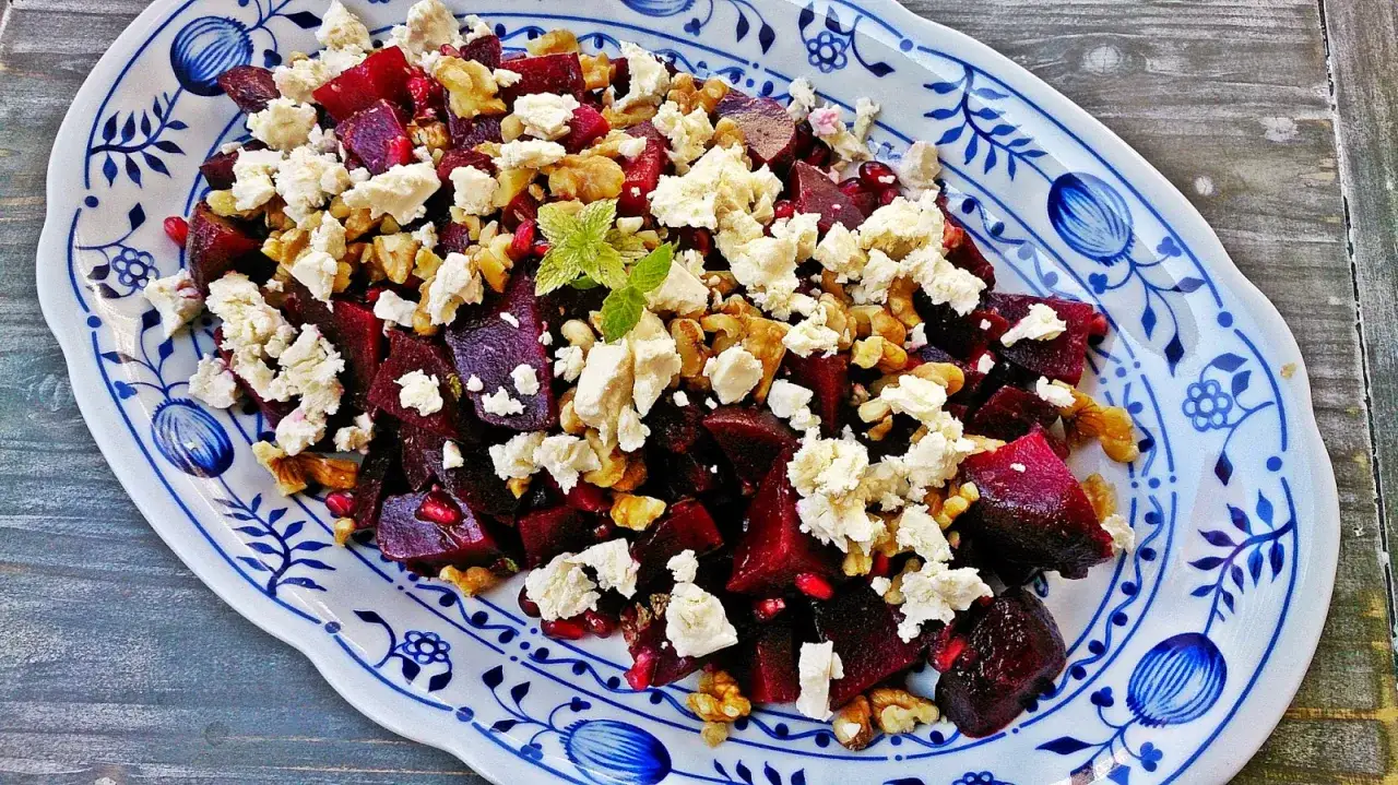 Ein bunter Rote Bete Feta Salat mit Waln&uuml;ssen und Granatapfelkernen, garniert mit Minze, auf einem blauen Zwiebelmuster-Teller.