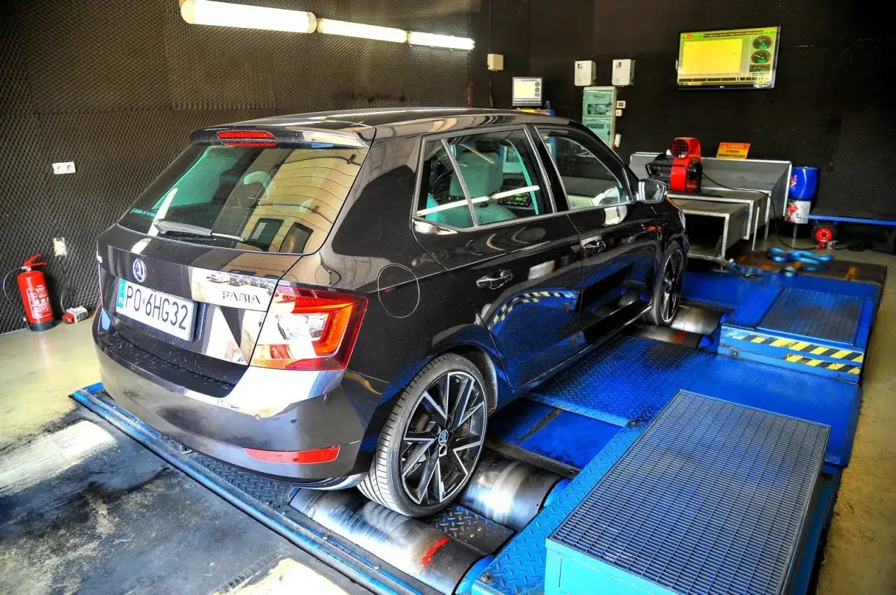 Czarna Skoda Fabia na hamowni, przygotowana do mapowania silnika. W tle widać sprzęt diagnostyczny i ekran z wykresami.