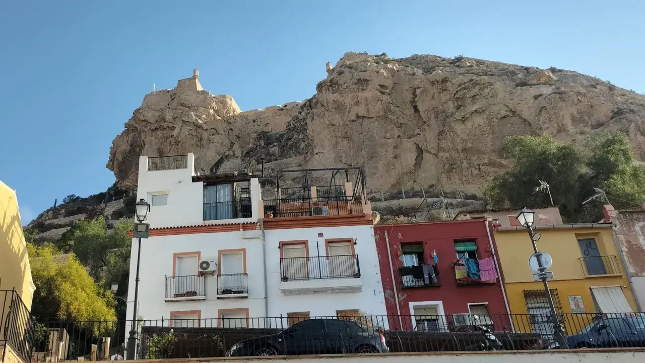 Edificios coloridos bajo el imponente Castillo de Santa Bárbara. ¡Una vista perfecta que ver en Alicante en un día!