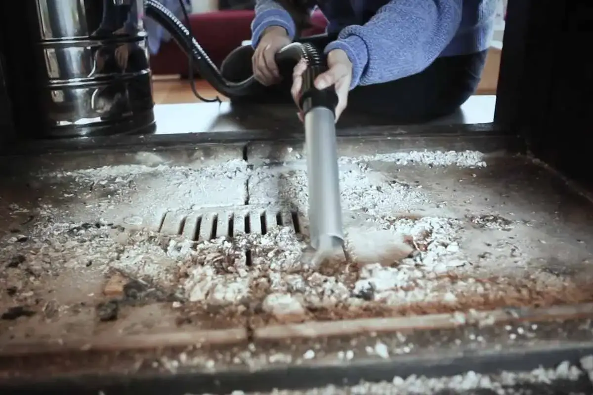 Une personne utilise un aspirateur normal pour aspirer les cendres d'une cheminée.