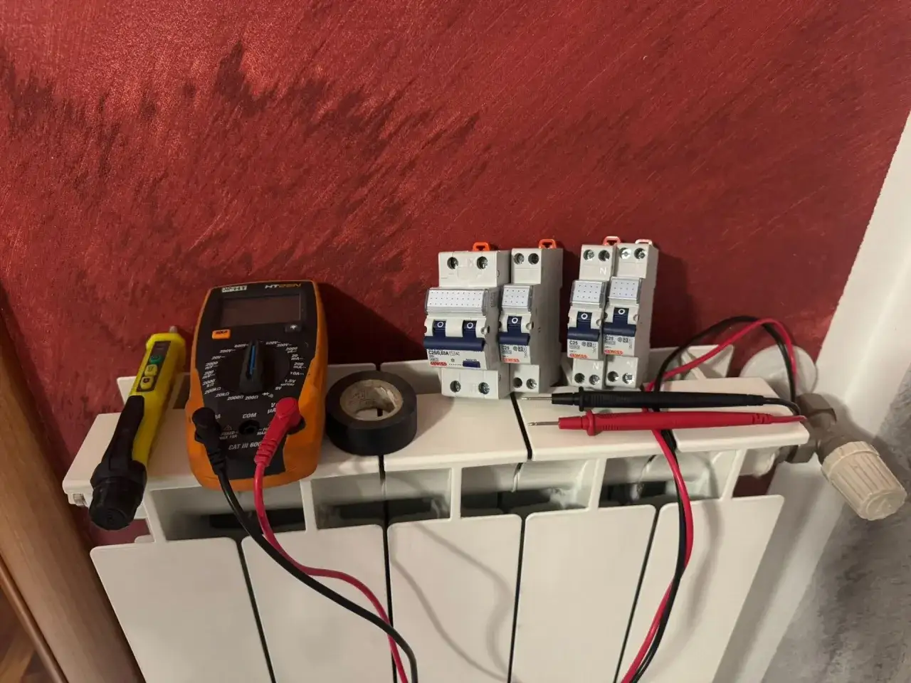 Strumenti per capire cosa fare se salta la corrente: multimetro, cercafase, interruttori e nastro isolante, pronti sul termosifone.
